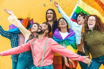 Diverse group of young people celebrating gay pride festival throwing confetti in the air - Lgbt community concept with guys and girls hugging together outdoors