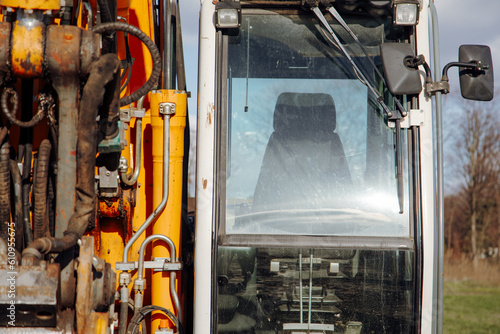 Vehicle cockpit of excavator, yellow metallic structure with transparent windshield. Operator's seat and controls ensure efficient operation on construction sites, ensuring safety and productivity