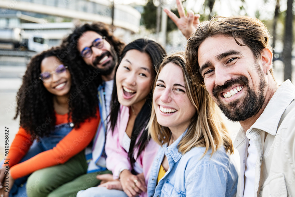 Diverse group of friends taking a selfie in the street sitting and looking at camera. Cheerful multiracial group of young hipsters taking a picture outside. Focus on front man and woman. Diverse group of friends taking a selfie in the street sitting and looking at camera. Cheerful multiracial group of young hipsters taking a picture outside. Focus on front man and woman.
