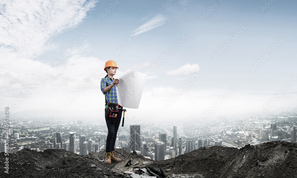 Obraz premium Female engineer in hardhat standing with blueprint