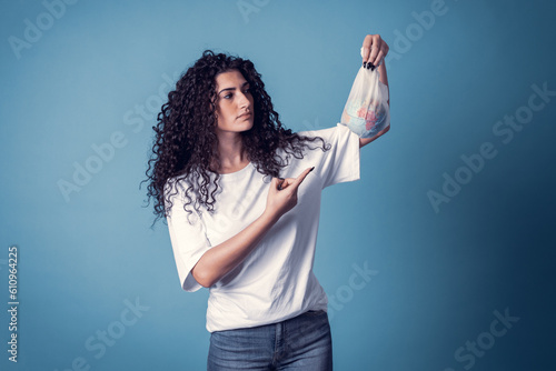 Studio shot of beautiful confident caucasian curly model woman wears blue jeans and casual basic solid white t-shirt, isolated over blue background. Pretty brunette holding small planet in her hands