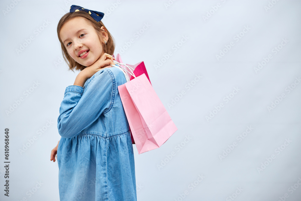 Pretty child girl in casual denim dress hold in hand pink shopping bags