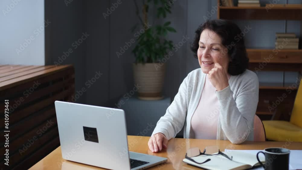 Happy middle aged senior woman sit with laptop talk on video call with friends family. Laughing mature old senior grandmother having fun talking speaking with grown up children online