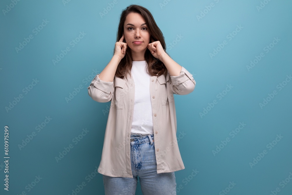 European model appearance young dark-haired lady in informal clothes closed her ear on a blue background European model appearance young dark-haired lady in informal clothes closed her ear on a blue background