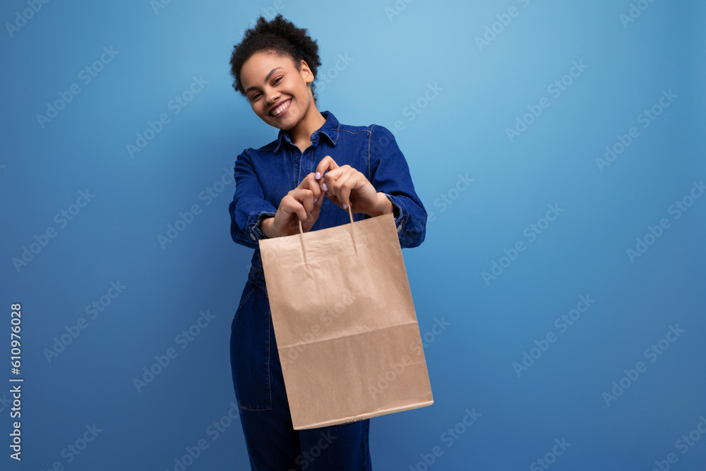 young successful woman with dark skin and black curly hair dressed in a blue denim suit holding a craft brown bag young successful woman with dark skin and black curly hair dressed in a blue denim suit holding a craft brown bag