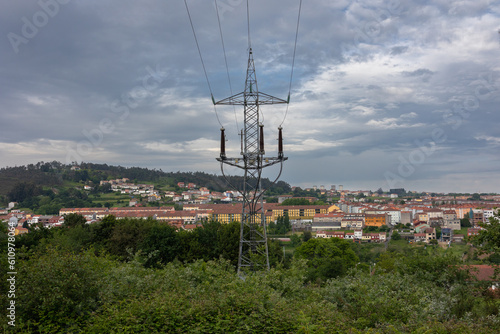 High-voltage tower against a cloudy sky. An electric line in the forest against the background of the city.