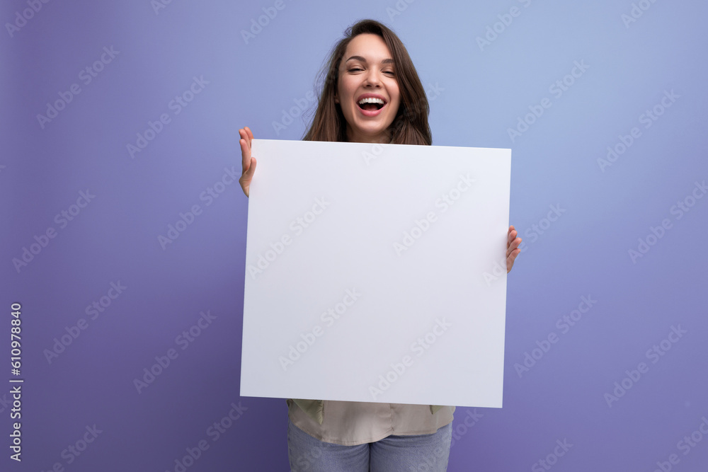 positive young brunette woman showing advertisement on white sheet - obrazy, fototapety, plakaty 