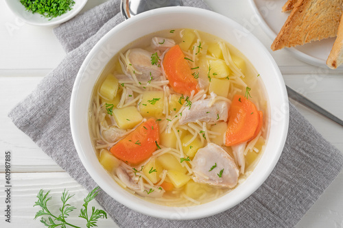 Chicken soup with noodles and vegetables in white bowl on a wooden background.