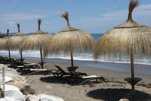 Empty beach with straw umbrellas and wooden beach beds with big stones on background on windy day.