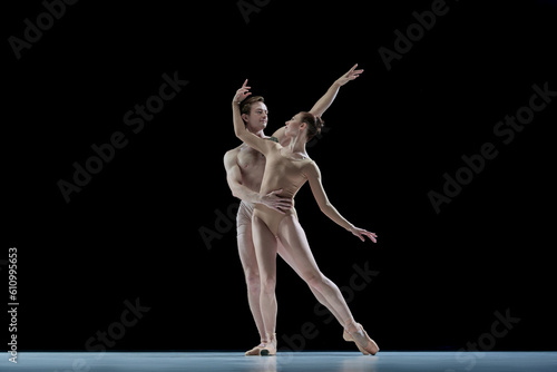 Passionate young couple, man and woman, ballet dancers in beige clothes dancing against black studio background. Concept of beauty, classical dance style, inspiration, movements. Ad