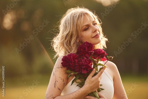 Portrait of beautiful young woman that is standing outdoors and holding red flowers