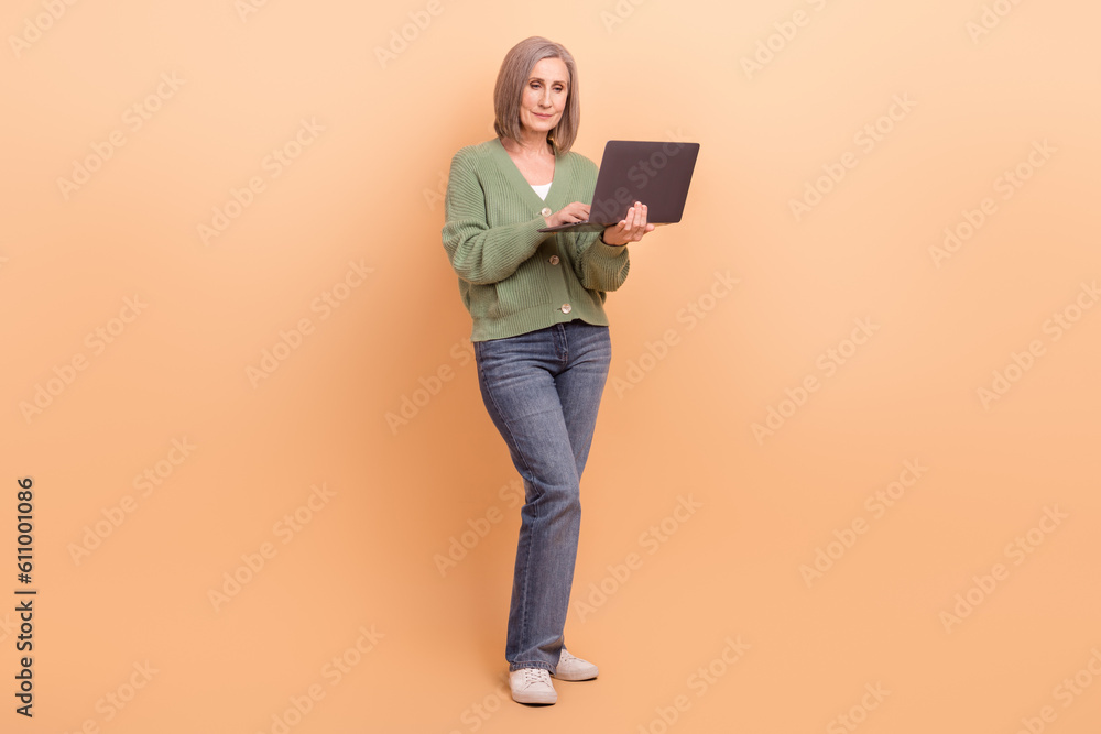 Full body size photo of confident team lead project manager retired businesswoman hold netbook coding isolated on beige color background Full body size photo of confident team lead project manager retired businesswoman hold netbook coding isolated on beige color background