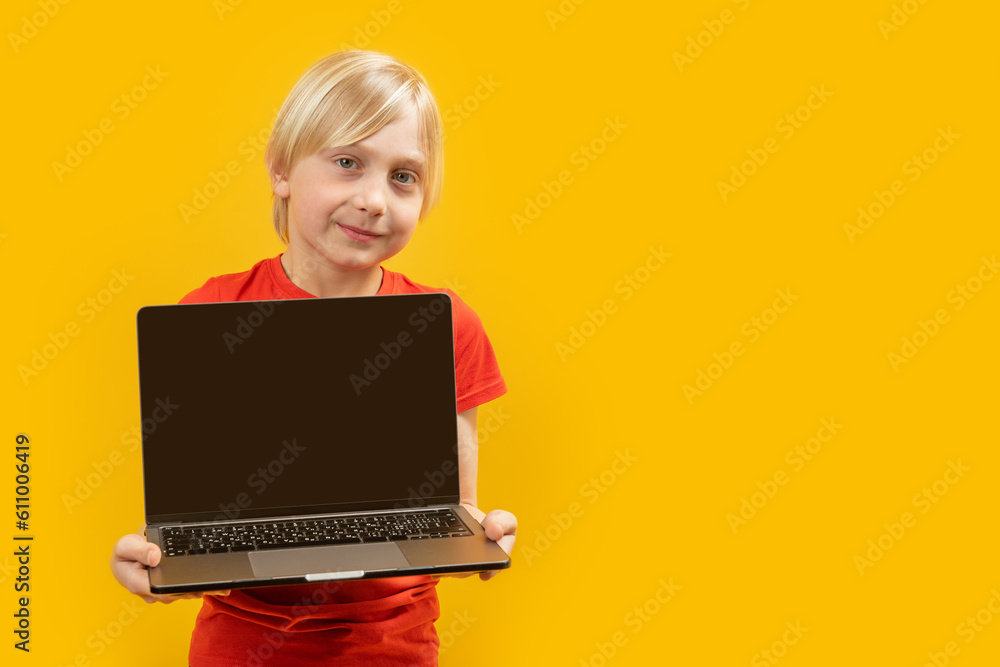 Naklejka premium Caucasian blond boy holds an open laptop with blank black screen. Studio photo of child with laptop. Copy space.
