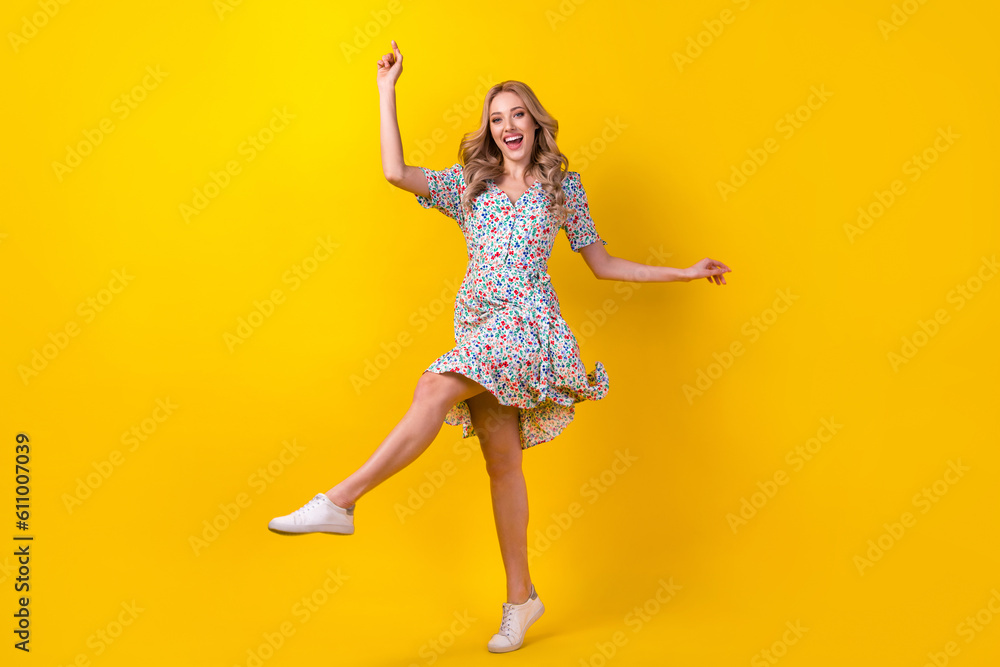 Full length photo of positive cheerful lady wear flower print dress having fun dancing isolated yellow color background Full length photo of positive cheerful lady wear flower print dress having fun dancing isolated yellow color background