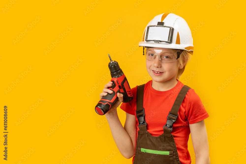 Portrait of boy as worker on yellow background. Child wears protective helmet and holds drill in his hand. Copy space, mock up Portrait of boy as worker on yellow background. Child wears protective helmet and holds drill in his hand. Copy space, mock up