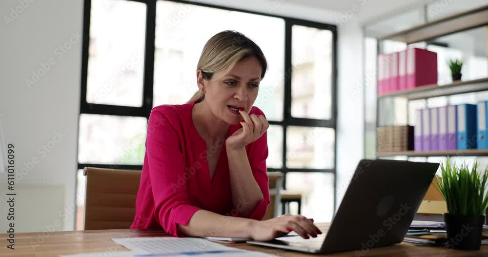 Worried woman using laptop gets nervous and loads nails. Anxious girl stressed by bad news in email and biting nails and looking at screen Worried woman using laptop gets nervous and loads nails. Anxious girl stressed by bad news in email and biting nails and looking at screen