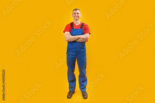 Happy builder workman crossing hands posing on yellow studio background. Copy Space. Full length portrait of worker.