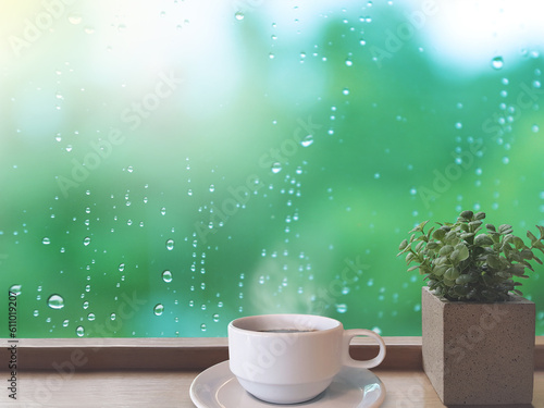 On a rainy day, water droplets were visible on the outside glass blurred. (Window background) The brown wooden floor on the left has white coffee cup and a plant pots.