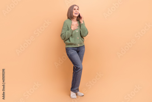 Full length photo of funny woman wear khaki cardigan arm on chest talk on smartphone look empty space isolated on beige color background