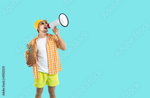 Funny young man in summer clothes and sunglasses hold pineapple scream in loudspeaker about discounts. Happy guy make announcement get attention using megaphone. Blue studio background.