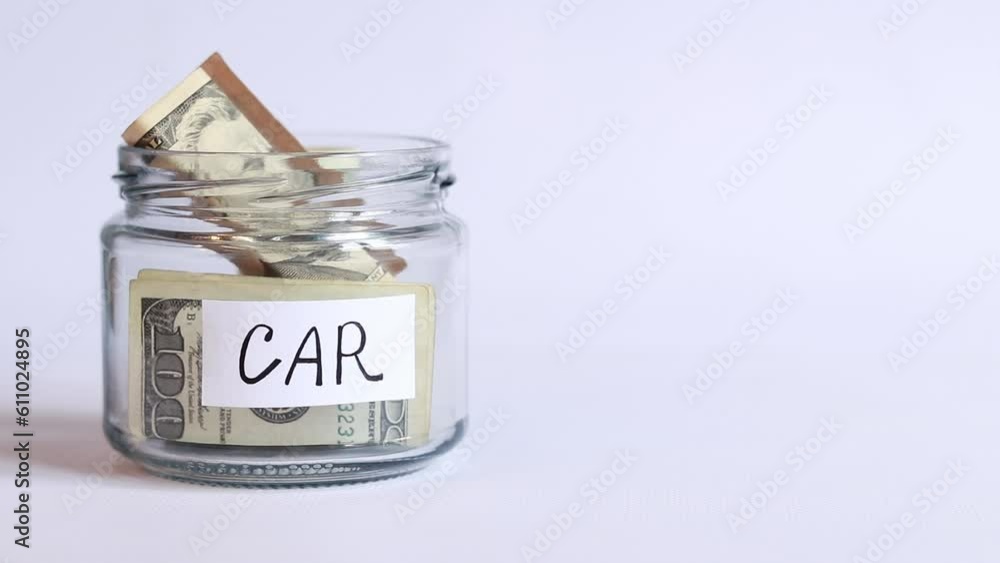 Glass jar with money on a white background close-up. Dollar bills fall into the jar. Piggy bank with dollars to buy a car. Accumulation of financial concept Glass jar with money on a white background close-up. Dollar bills fall into the jar. Piggy bank with dollars to buy a car. Accumulation of financial concept