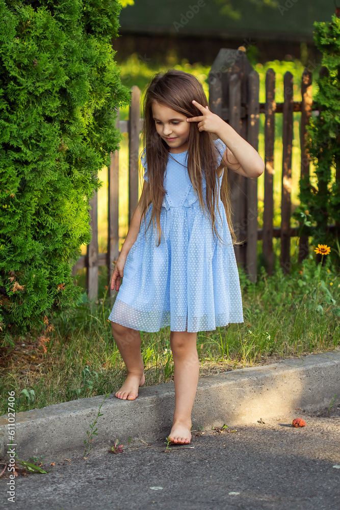 Little beautiful girl in a blue dress barefoot in the summer on the street Little beautiful girl in a blue dress barefoot in the summer on the street
