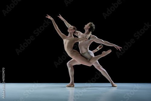 Talented, artistic young couple, man and woman, ballet dancers making impressive performance against black studio background. Concept of beauty, classical dance style, inspiration, movements. Ad