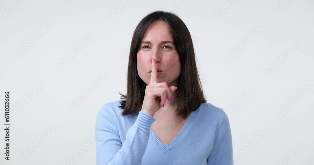 A Caucasian woman standing on a white background looks around carefully and shows a Shhh gesture by placing her finger on lips. With a wide smile on her face, she seems excited to share some gossip. A Caucasian woman standing on a white background looks around carefully and shows a Shhh gesture by placing her finger on lips. With a wide smile on her face, she seems excited to share some gossip.