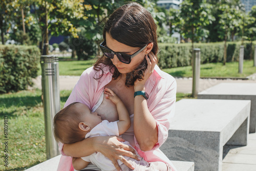 a young mother in a pink shirt breastfeeds her baby on a bench in the park on a sunny summer warm day