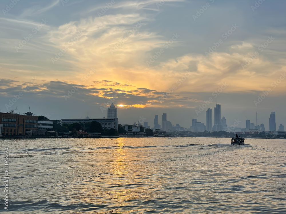 City skyline. Magnificent sunset over Bangkok city, Chao Phraya river. Floating boat moves off into the distance, leaving footprints on water. Beautiful sky with bright glow of sun, pattern of clouds.