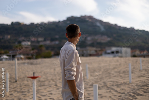 young caucasian man with collarless shirt and dress pants, on the beach looking back © emanuel nyszczuk