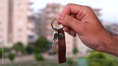 Man showing keys to a new house in front of blurred condos, the image of the house key used for real estate ads
