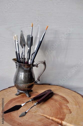 Wooden tree stump platform on which there is a little silvery jug, art supplies, brushes and spatulas.