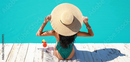 Beautiful young woman with cocktail sitting near swimming pool at tropical resort, back view