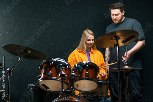 young girl in a drum school learns to play a musical instrument with a teacher rehearsing in a band's music studio