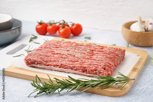 Board with fresh minced meat, rosemary and tomatoes on grey grunge background