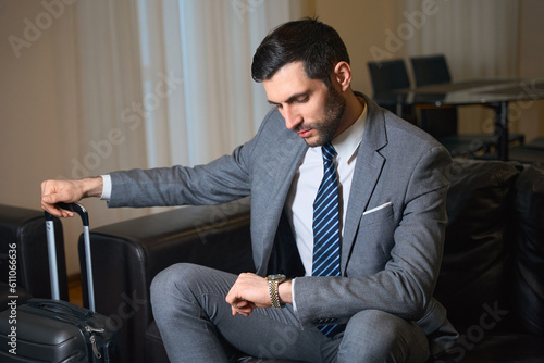 Elegant man sits on leather sofa and looks at his wristwatch