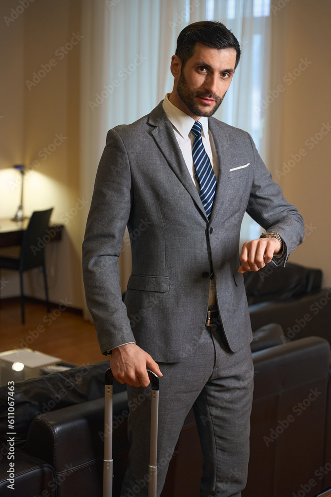 Fototapeta premium Businessman with a travel suitcase stands in a hotel room