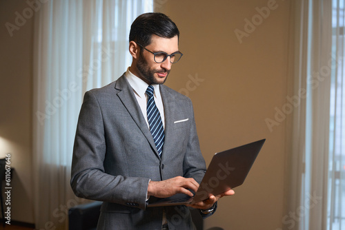 Elegant brunette is standing in a hotel room with laptop