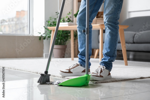 Fotografi Young man sweeping floor with broom at home