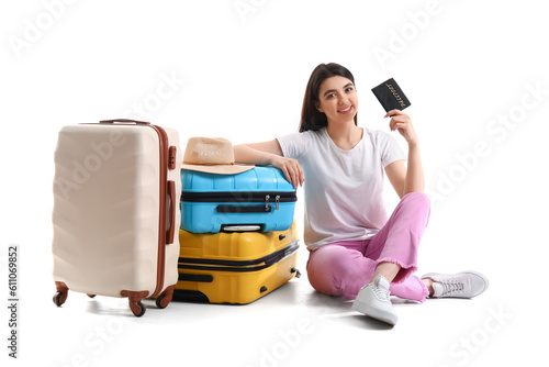 Young woman with passport and suitcases sitting on white background