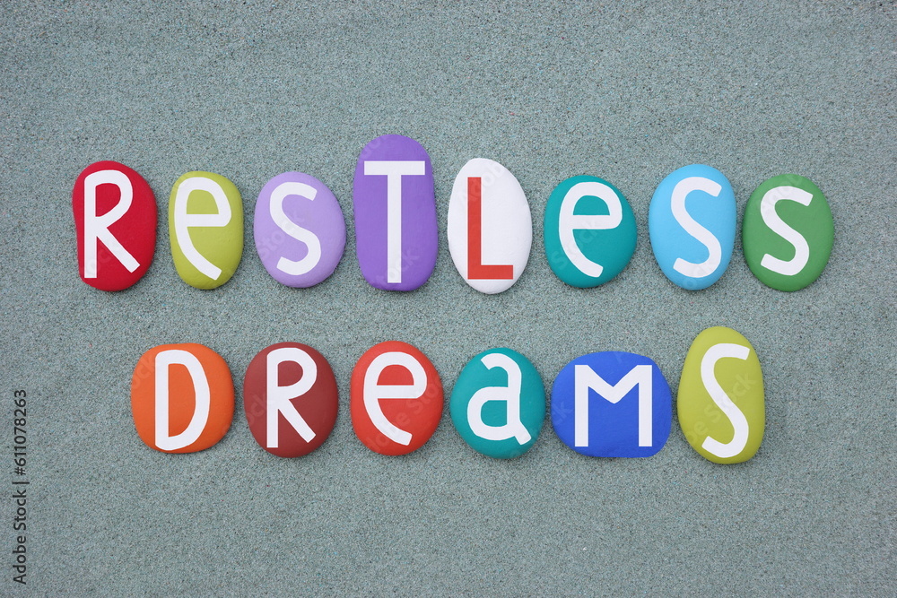 Restless Dreams, creative text composed with multi colored stone letters over green sand Restless Dreams, creative text composed with multi colored stone letters over green sand