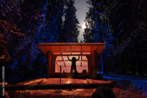 Woman at forest shelter in winter firelight under full moon 