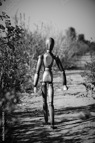 Wooden mannequin walking along path among vegetation in black and white photo.
