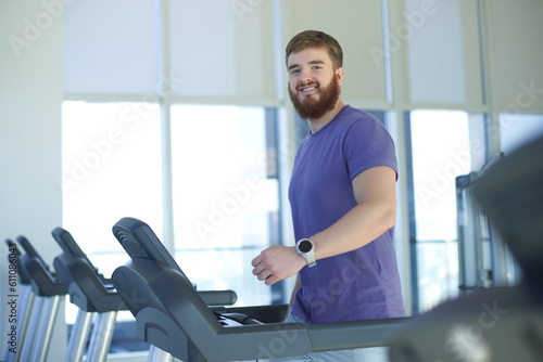 Happy young fit man training in the gym, running jogging on treadmill, doing cardio exercise and smile. Healthy lifestyle, sport, fitness concept