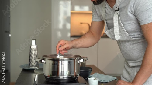 Wallpaper Mural Man stirs boiling soup with spoon in pot on stove and tastes on background of home kitchen. Cooking food Torontodigital.ca