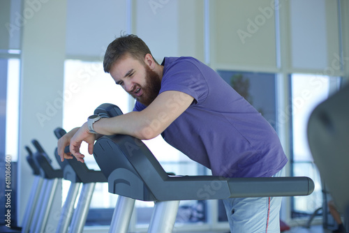 Tired exhausted young man feeling bad, unhealthy, unwell during run on treadmill in the gym photo