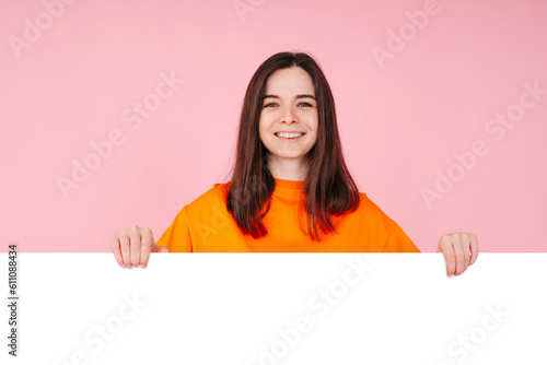 Surprised Woman Holding White Promo Paper, Excited by Unexpected Best Deal Offer. Isolated on Pink Background. Perfect for Marketing, Promotions, Sales, and Advertising Concepts