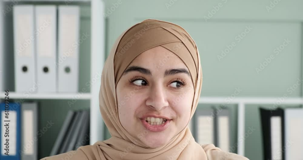 Young Arab woman wearing a hijab as she engages in a video call. With a cheerful demeanor and a radiant smile. Directly looking into the camera, she establishes a personal connection. Young Arab woman wearing a hijab as she engages in a video call. With a cheerful demeanor and a radiant smile. Directly looking into the camera, she establishes a personal connection.