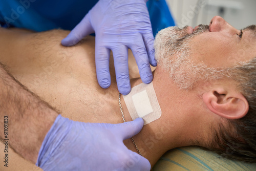 Man doctor sticking patch to patient neck after injection